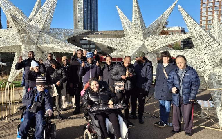 Walking group including disabled and non-disabled people smiling for a photo in front of an arti installation of stars